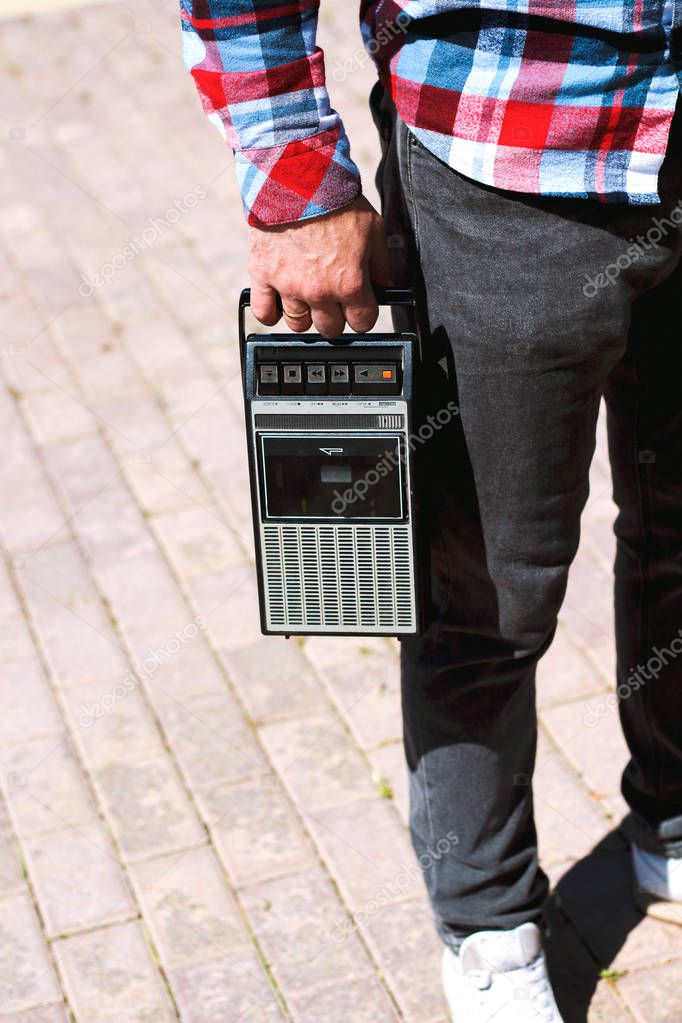 Hipster fancy man in plaid shirt holding in hand and walking with retro vintage old 80s , 90s style portable radio audio cassette recorder player boombox with audio tape cassette inside 