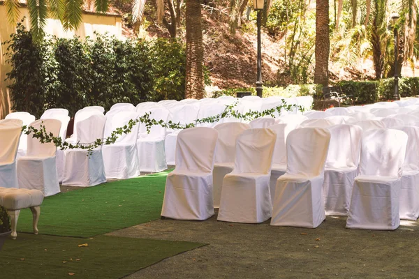 rows of chairs in white capes for guests at a wedding ceremony event outside in the park in the shade of trees, a romantic place under a canopy