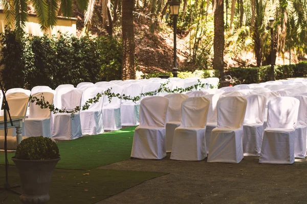rows of chairs in white capes for guests at a wedding ceremony event outside in the park in the shade of trees, a romantic place under a canopy