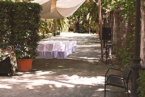 rows of chairs in white capes for guests at a wedding ceremony event outside in the park in the shade of trees, a romantic place under a canopy