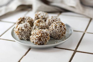 vejetaryen çiğ sağlıklı diyet hiçbir fırında şeker topları tatlı tatlılar şekersiz glutensiz hindistan cevizi gevreği ile, beyaz bir kiremit arka plan üzerinde mavi plaka üzerinde uygun beslenme snack, yumuşak seçici odak