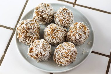 vejetaryen çiğ sağlıklı diyet hiçbir fırında şeker topları tatlı tatlılar şekersiz glutensiz hindistan cevizi gevreği ile, beyaz bir kiremit arka plan üzerinde mavi plaka üzerinde uygun beslenme snack, yumuşak seçici odak