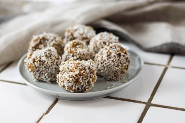 vejetaryen çiğ sağlıklı diyet hiçbir fırında şeker topları tatlı tatlılar şekersiz glutensiz hindistan cevizi gevreği ile, beyaz bir kiremit arka plan üzerinde mavi plaka üzerinde uygun beslenme snack, yumuşak seçici odak