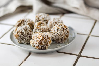 vejetaryen çiğ sağlıklı diyet hiçbir fırında şeker topları tatlı tatlılar şekersiz glutensiz hindistan cevizi gevreği ile, beyaz bir kiremit arka plan üzerinde mavi plaka üzerinde uygun beslenme snack, yumuşak seçici odak