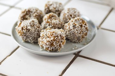 vejetaryen çiğ sağlıklı diyet hiçbir fırında şeker topları tatlı tatlılar şekersiz glutensiz hindistan cevizi gevreği ile, beyaz bir kiremit arka plan üzerinde mavi plaka üzerinde uygun beslenme snack, yumuşak seçici odak