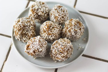 vejetaryen çiğ sağlıklı diyet hiçbir fırında şeker topları tatlı tatlılar şekersiz glutensiz hindistan cevizi gevreği ile, beyaz bir kiremit arka plan üzerinde mavi plaka üzerinde uygun beslenme snack, yumuşak seçici odak