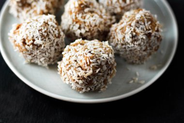vejetaryen çiğ sağlıklı diyet hiçbir fırında şeker topları tatlı tatlılar şekersiz glutensiz hindistan cevizi gevreği ile, beyaz bir kiremit arka plan üzerinde mavi plaka üzerinde uygun beslenme snack, yumuşak seçici odak