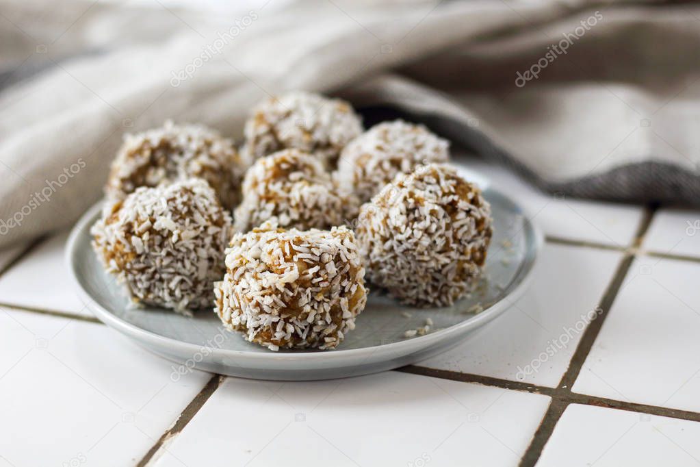 vegetarian raw healthy diet  no bake candies balls dessert sweets sugar free gluten-free with coconut flakes, proper nutrition snack on blue plate on a white tile background, soft selective focus
