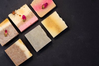 metin için boş bir alan ile siyah bir arka plan üzerinde otlar ve gül tomurcukları ile el yapımı çok renkli sabun. Yüz ve vücut tedavileri için spa sabunu düz yatıyordu istagram tarzı