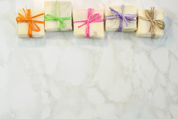 handmade organic soap in gift wax wrapping  paper with multi colored eco raffia ribbons on marble surface with space for text. Instagram style soap flat lay frame