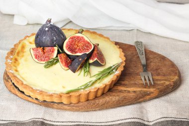 muhteşem yuvarlak fransız klasik ev yapımı shortcake pasta hamuru vanilyalı muhallebi tart kek gri masa örtüsü üzerinde retro çatal ile yakın ahşap plaka üzerinde incir ve biberiye ile süslenmiş. Insta yemek tarzı