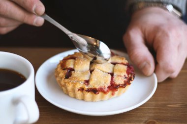 Gri kazaklı adam kışın kahve dükkanında siyah lungo americano kahvesi içer ve ahşap masada beyaz tabakta Amerikan ev yapımı vişneli turta yer. Sonbahar ruh hali instagram biçimi