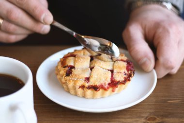 Gri kazaklı adam kışın kahve dükkanında siyah lungo americano kahvesi içer ve ahşap masada beyaz tabakta Amerikan ev yapımı vişneli turta yer. Sonbahar ruh hali instagram biçimi