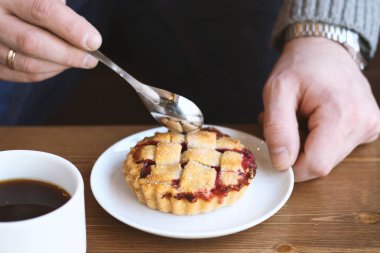 Gri kazaklı adam kışın kahve dükkanında siyah lungo americano kahvesi içer ve ahşap masada beyaz tabakta Amerikan ev yapımı vişneli turta yer. Sonbahar ruh hali instagram biçimi