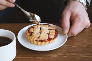 Gri kazaklı adam kışın kahve dükkanında siyah lungo americano kahvesi içer ve ahşap masada beyaz tabakta Amerikan ev yapımı vişneli turta yer. Sonbahar ruh hali instagram biçimi