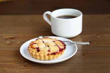 Gri kazaklı adam kışın kahve dükkanında siyah lungo americano kahvesi içer ve ahşap masada beyaz tabakta Amerikan ev yapımı vişneli turta yer. Sonbahar ruh hali instagram biçimi