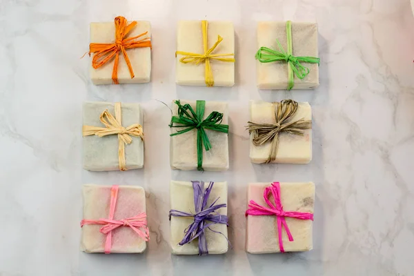 handmade organic craft soap in gift wax wrapping  paper with multi colored eco raffia ribbons on marble surface with space for text. Present gift soap flat lay top view2