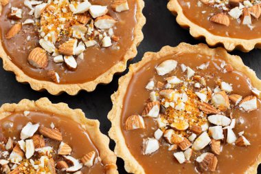 Kısa kek sucre hamur tatlısı karamel tartlı karamelli tart, karamelli pasta, fındık, badem, karamelli ekmek kırıntıları siyah bir tabakta. Kutlama için en iyi manzara porsiyonlu tatlı