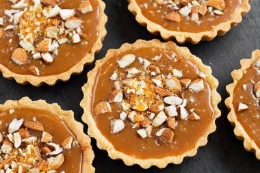 Kısa kek sucre hamur tatlısı karamel tartlı karamelli tart, karamelli pasta, fındık, badem, karamelli ekmek kırıntıları siyah bir tabakta. Kutlama için en iyi manzara porsiyonlu tatlı