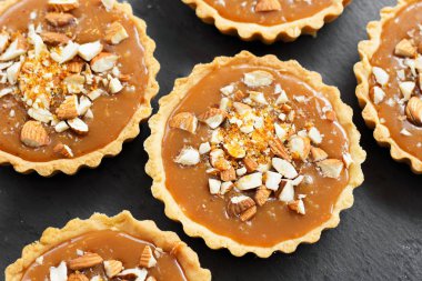 Kısa kek sucre hamur tatlısı karamel tartlı karamelli tart, karamelli pasta, fındık, badem, karamelli ekmek kırıntıları siyah bir tabakta. Kutlama için en iyi manzara porsiyonlu tatlı