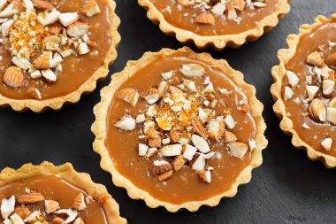 Kısa kek sucre hamur tatlısı karamel tartlı karamelli tart, karamelli pasta, fındık, badem, karamelli ekmek kırıntıları siyah bir tabakta. Kutlama için en iyi manzara porsiyonlu tatlı