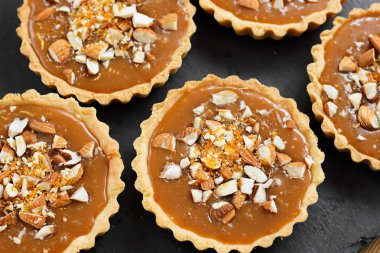 Kısa kek sucre hamur tatlısı karamel tartlı karamelli tart, karamelli pasta, fındık, badem, karamelli ekmek kırıntıları siyah bir tabakta. Kutlama için en iyi manzara porsiyonlu tatlı