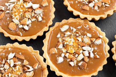 Kısa kek sucre hamur tatlısı karamel tartlı karamelli tart, karamelli pasta, fındık, badem, karamelli ekmek kırıntıları siyah bir tabakta. Kutlama için en iyi manzara porsiyonlu tatlı