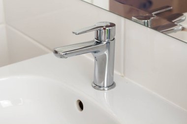 Gümüş metal, parlak musluk musluğu ve büyük aynalı seramik lavabo. Otel evindeki spa banyosunda duvarında beyaz fayanslar var. Banyo, lüks bir yer. Yumuşak seçili bulanık odak 