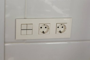 İki beyaz soket ve duvarda anahtar. Otel banyosunda fayanslar ve duvarda beyaz fayanslar var. Banyo lüks iç mekan. 