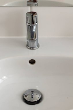 Gümüş metal, parlak musluk musluğu ve büyük aynalı seramik lavabo. Otel evindeki spa banyosunda duvarında beyaz fayanslar var. Banyo, lüks bir yer. Yumuşak seçili bulanık odak 