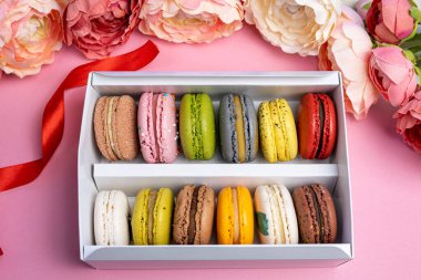 Pembe kutlama partisinde hediye kutusundaki renkli modern badem kurabiyeleri romantik parti, pion çiçekleri, saten kurdele, bir sürü çeşit makaron. Yumuşak düz üst görünüm