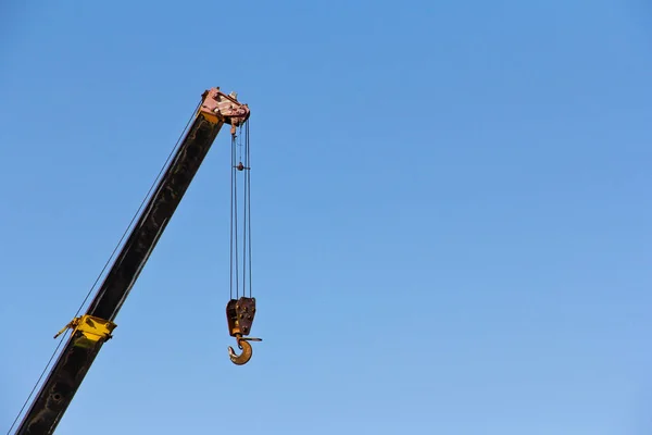 Crane boom with hooks isolated on a blue sky background. Lifting equipment at a construction site. Special machinery.