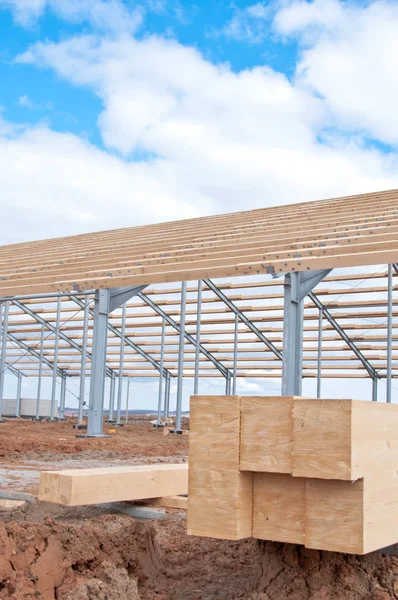 Metal frame of the new building against the blue sky with clouds. Metal frame of the building for further insulation. Wood beams and metal frame of the new building. The use of two materials in construction. Wood and metal at a construction site.