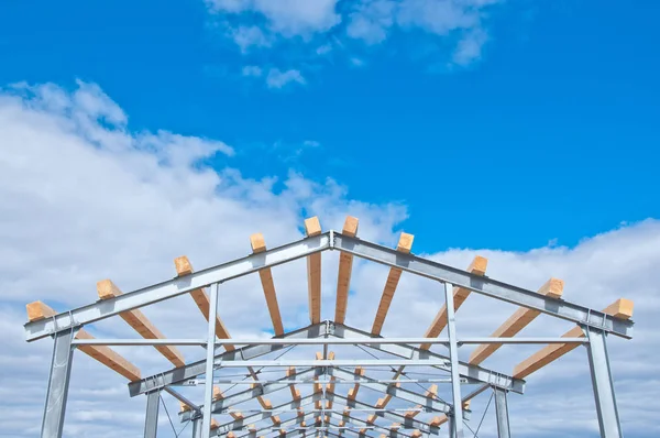 Metal frame of the new building against the blue sky with clouds. Metal frame of the building for further insulation. Wood beams and metal frame of the new building. The use of two materials in construction. Wood and metal at a construction site.