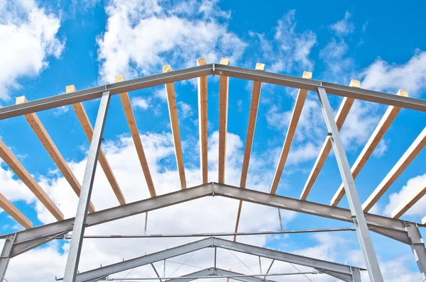 Metal frame of the new building against the blue sky with clouds. Metal frame of the building for further insulation. Wood beams and metal frame of the new building. The use of two materials in construction. Wood and metal at a construction site.