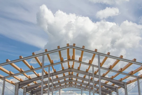 Wooden beams on the metal frame of the building against the blue sky. Roofing during the construction of the hangar.