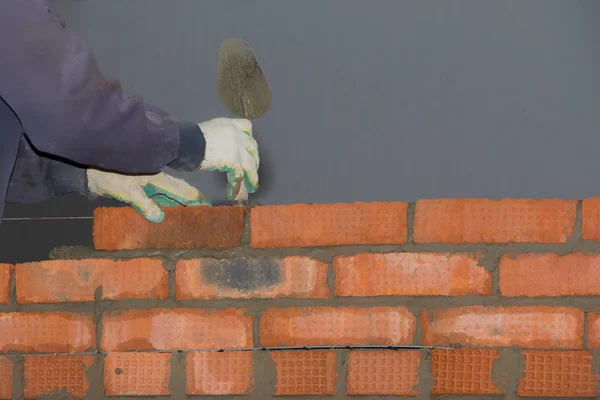 Hands of a bricklayer laying down a row on masonry.