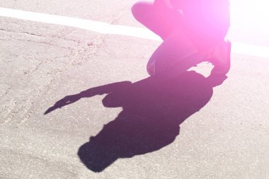 Genç bir adam akıllı telefonuyla kaldırımda çömeliyor ve gölgesi var. Ayarlanmış