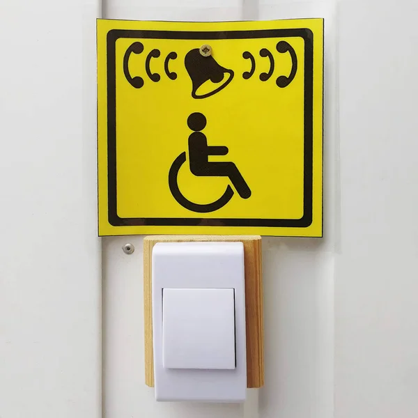 Handicapped call button and yellow sign with icon on white wall
