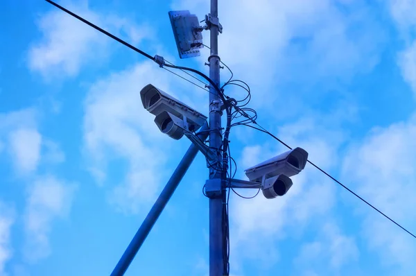 青空と雲に対する市内のポール上の2台の監視カメラと送信機 — ストック写真