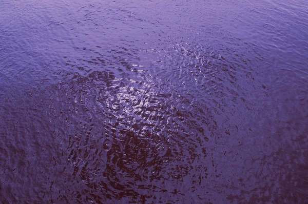 The water in the river with a purple tint and a glare of the sun. Top view from the front.