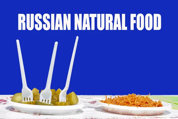 食べ物と2つのプラスチックプレート 一つは スライスされたキュウリと3つのプラスチックフォーク 他のすりおろしたニンジンで 碑文の上に ロシアの自然食品 青い背景 正面図 — ストック写真