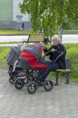 Büyükbaba torunları ile iki bebek arabası sallar. Cephe görünümü, Surgut, Rusya - 12 Haziran 2019