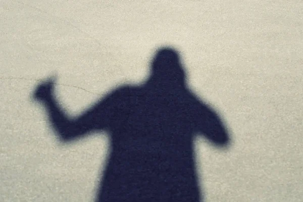 Shadow of a man on the pavement with a camera in his hands and shows a thumb up. Top view of the front.