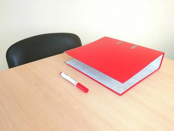 Office.  Table.  On the table is a red folder and a red marker.  Front side view.