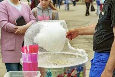 Bir erkek satıcı makinede pamuk şeker hazırlıyor. Anne ve kız alıcılar bekliyor. Surgut, Rusya - 12 Haziran 2019.
