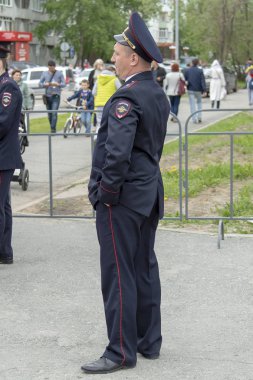Sokakta bir polis duruyor, elleri pantolonunun cebinde. Yoldan geçen insanlara yakından bakıyor. Surgut, Rusya - 12 Haziran 2019.