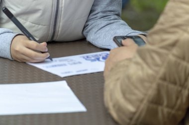 Çocuk masanın üzerinde duran bir kağıt parçasına keçeli kalemle resim çizer. Aksine, bir yetişkin akıllı telefon tutar. Ön görünüm.