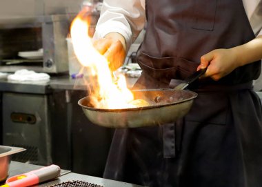 Şef bir tavada bir mutfak soba, soba pan ile Restoran mutfakta Şef üzerinde alev ile pişirme