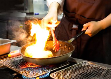 Şef bir tavada bir mutfak soba, soba pan ile Restoran mutfakta Şef üzerinde alev ile pişirme